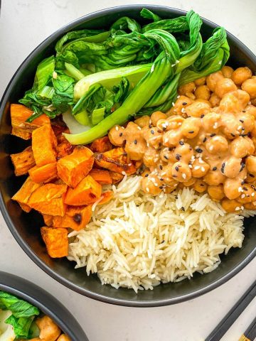 Black bowl with rice, chickpeas in peanut sauce, bok choy and sweet potato cubes.