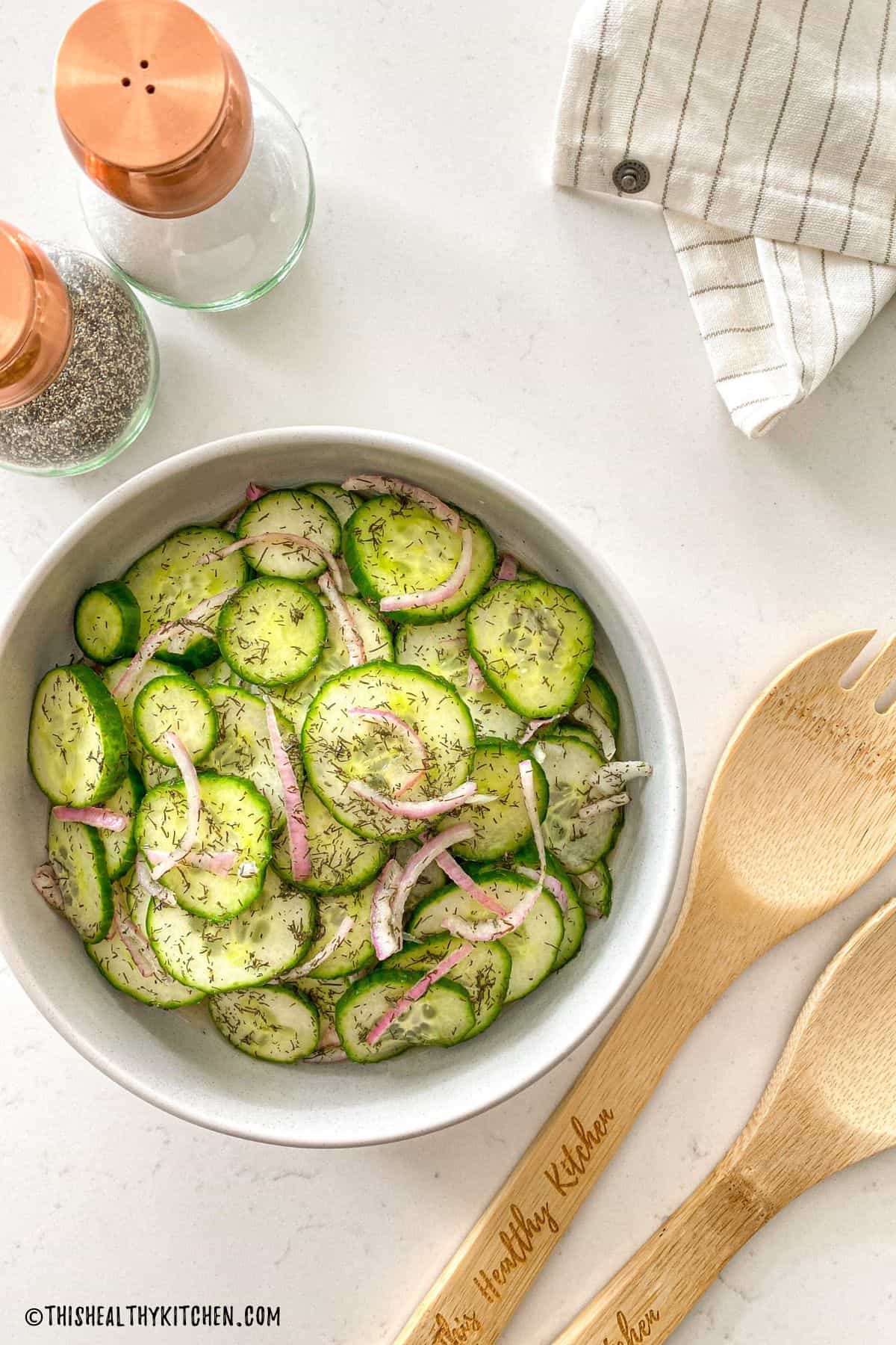 Cucumber salad with dill in serving bowl with salt and pepper shakers above it.