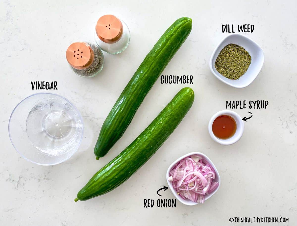 Cucumber, vinegar, dill, maple syrup, and red onion on kitchen counter top.