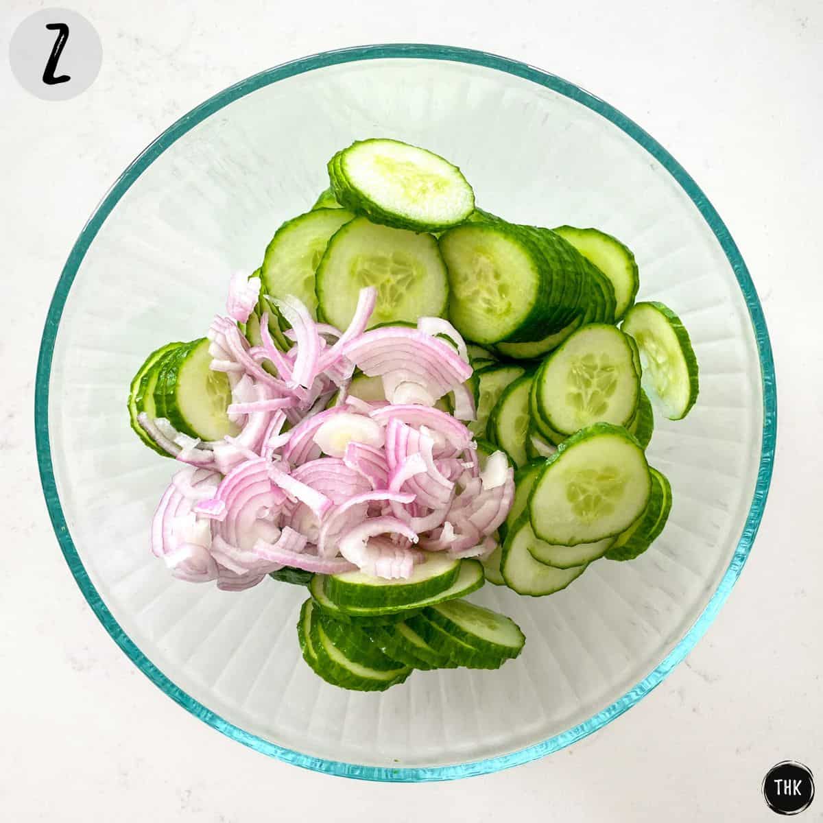 Cucumber slices and red onion in large glass bowl.