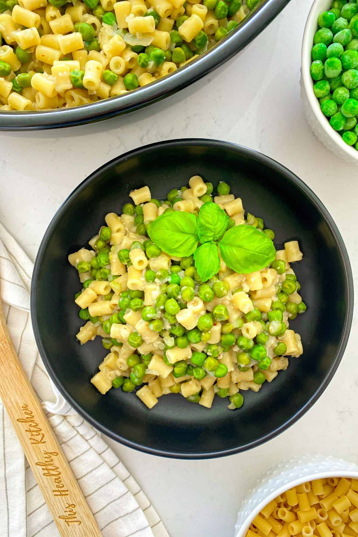 Black bowl with pasta and peas inside with basil leaf garnish.