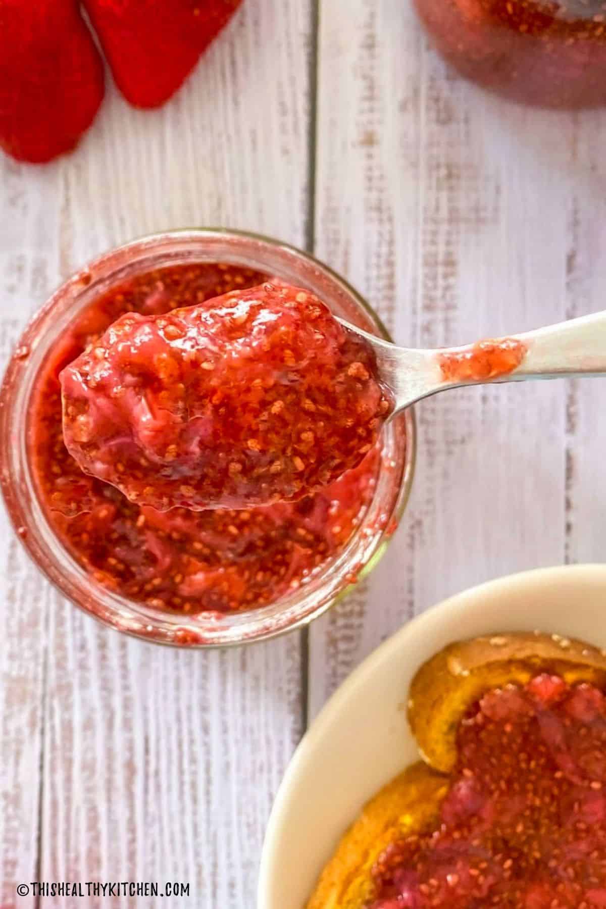 A spoonful of strawberry jam being held above the jar.
