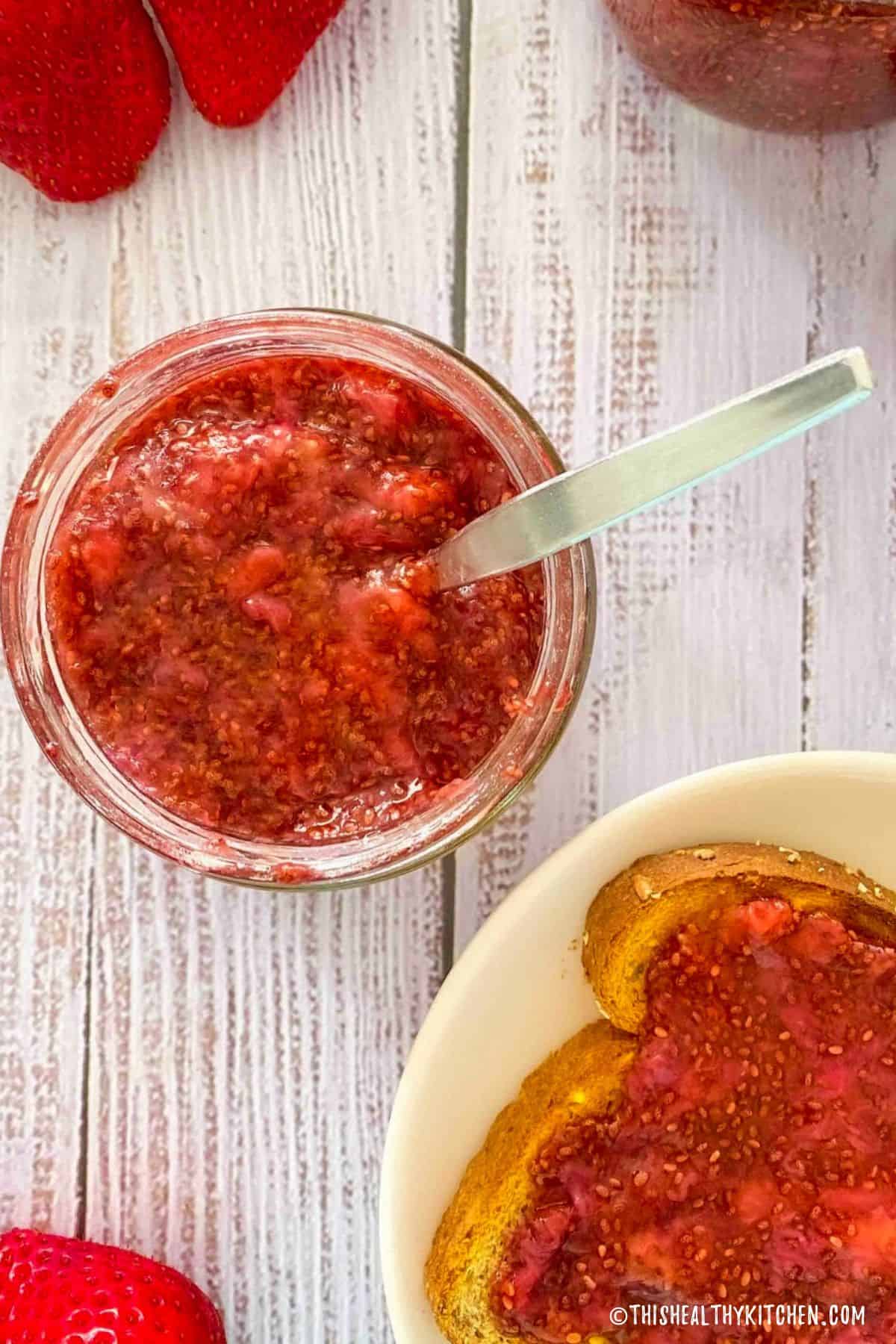 Jar of strawberry jam and toast with jam on top below it.