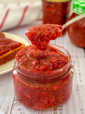 Spoonful of strawberry jam being held above the jar.
