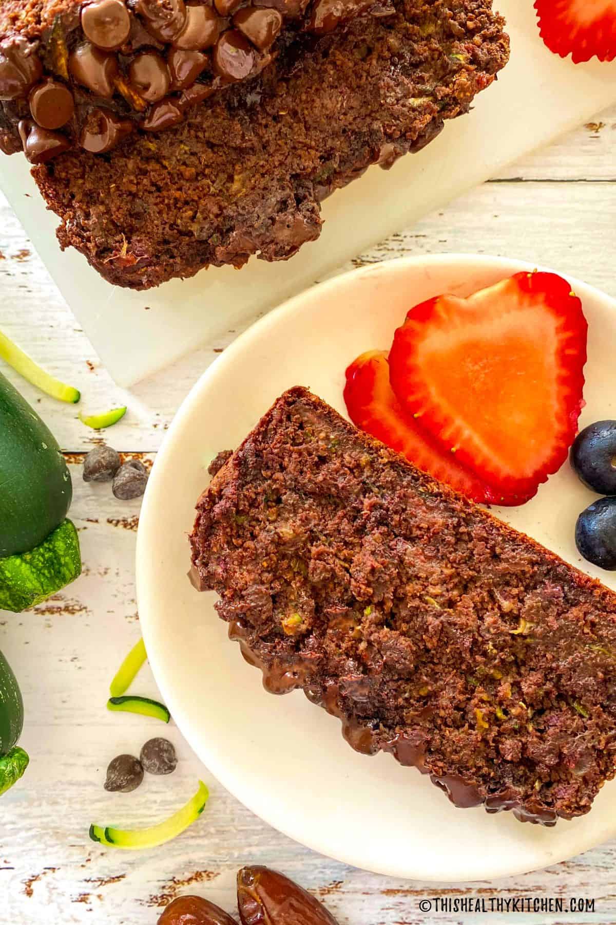 Slice of chocolate zucchini bread in plate with strawberries and blueberries beside it.