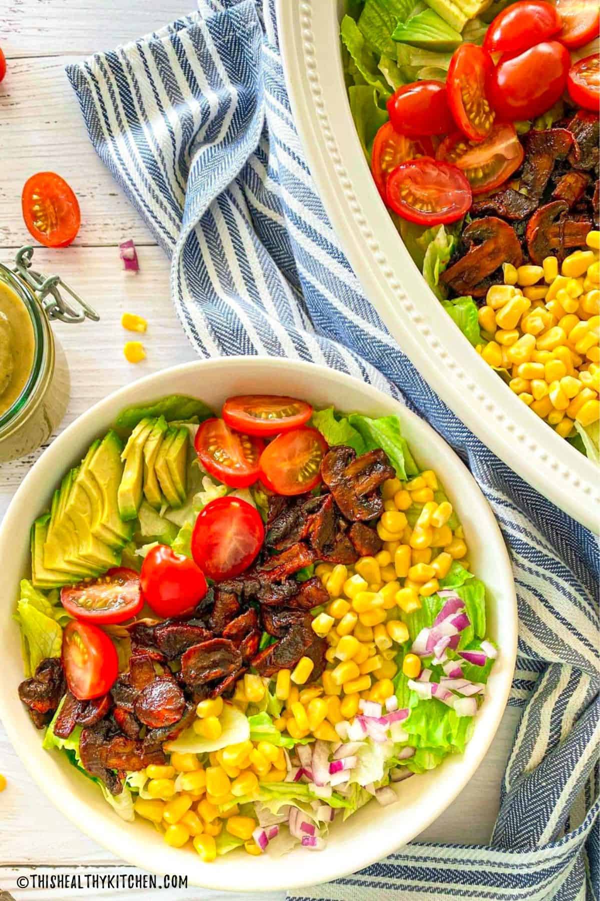 Salad with red onion, corn, mushrooms, tomatoes, and avocado on top.