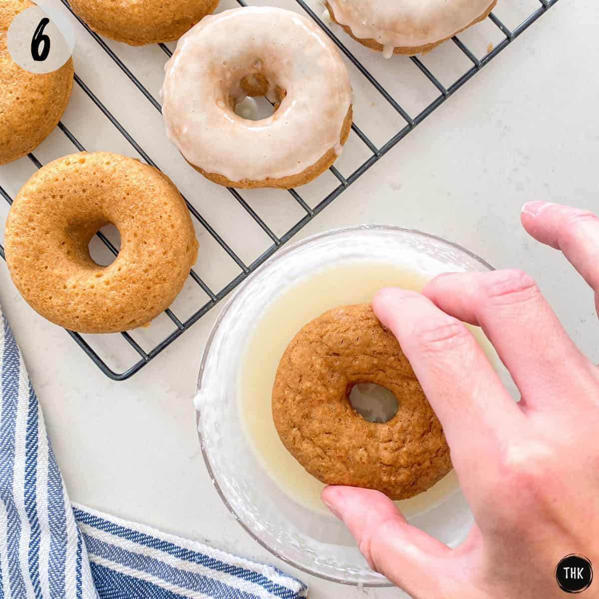Donut being dipped into bowl of glaze.