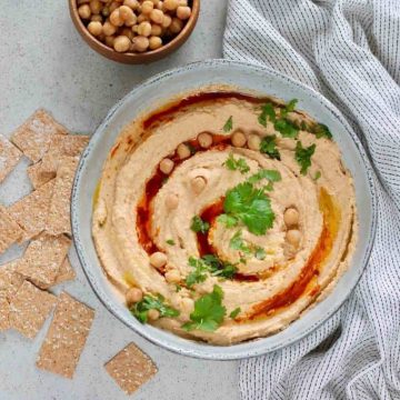 Bowl of spicy hummus with crackers around it.