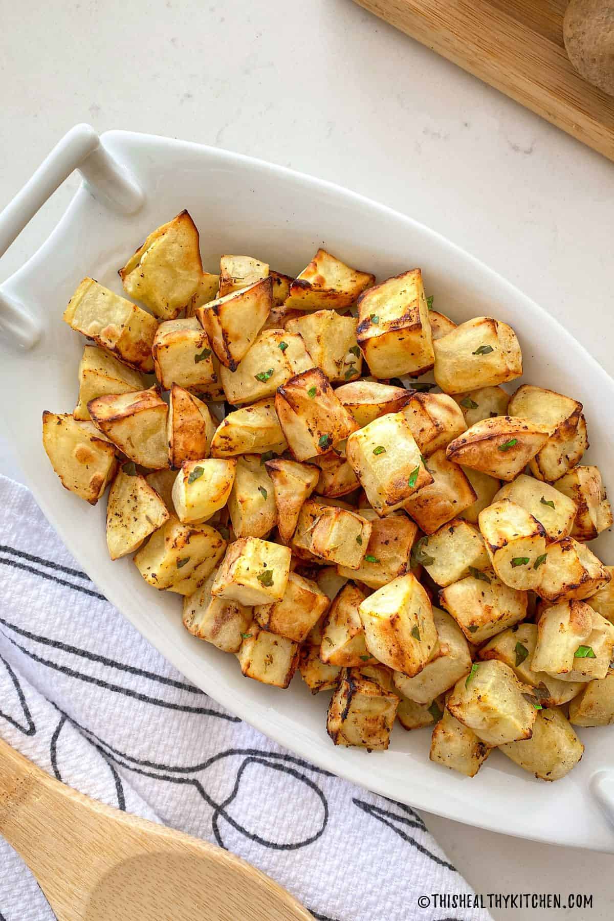 Crispy cubed potatoes in serving dish with chopped parsley on top.