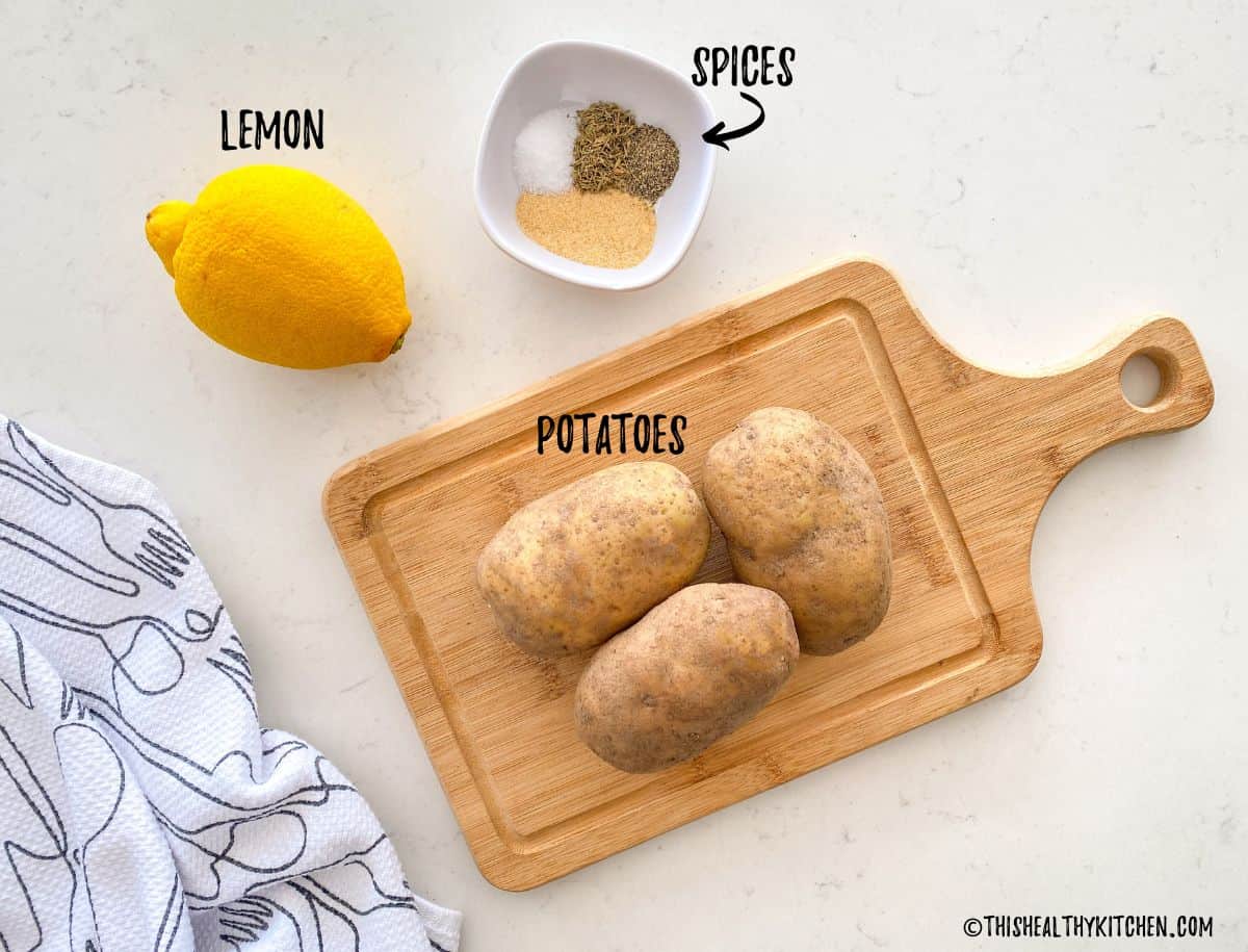 Potatoes on cutting board with spices in a prep bowl and lemon beside it.