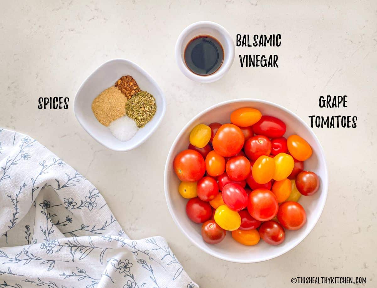 Bowl of grape tomatoes, bowl of spices, and bowl of balsamic vinegar on kitchen countertop.