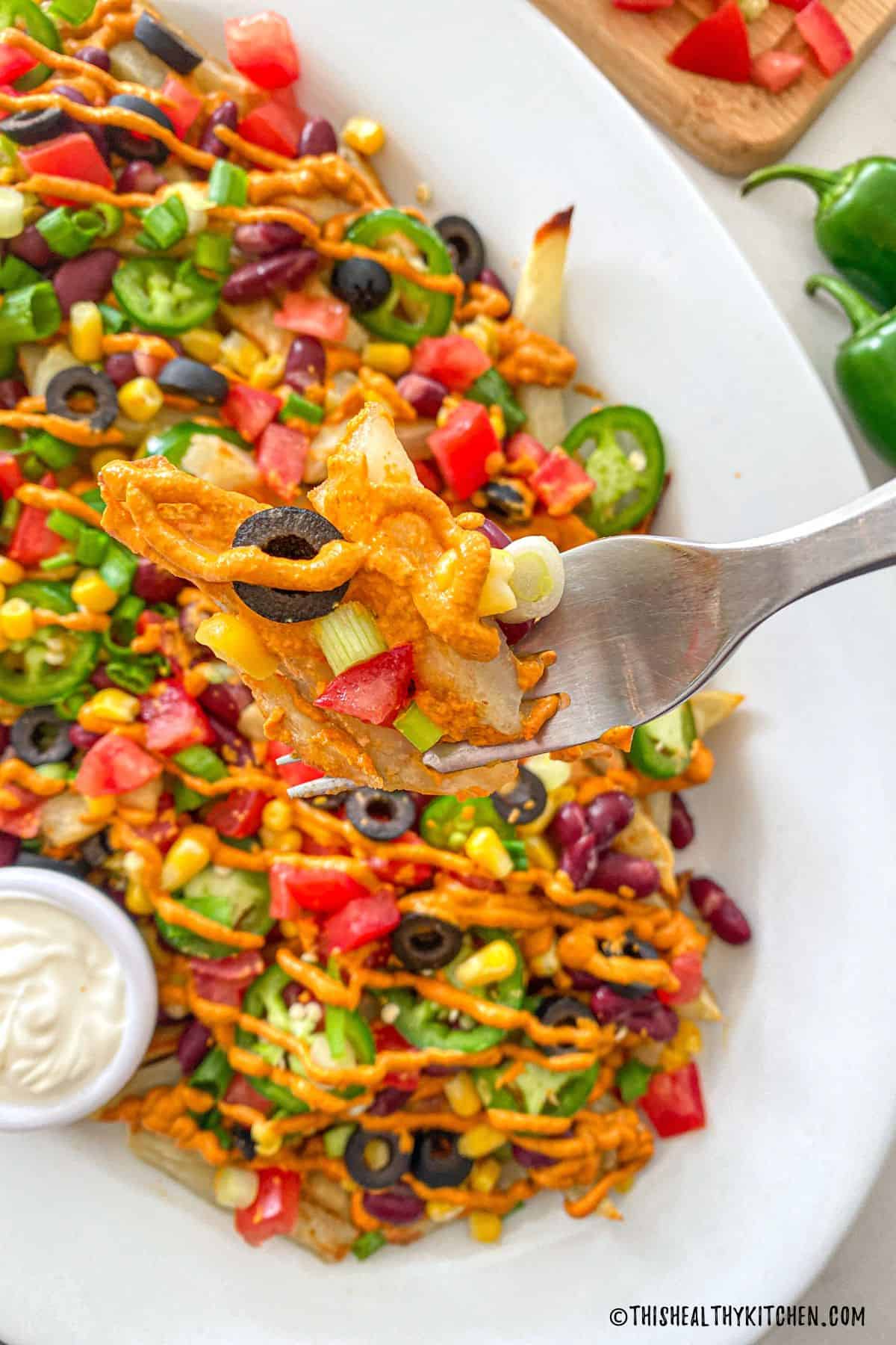 Fork full of french fries with cheese sauce and nacho toppings on them.
