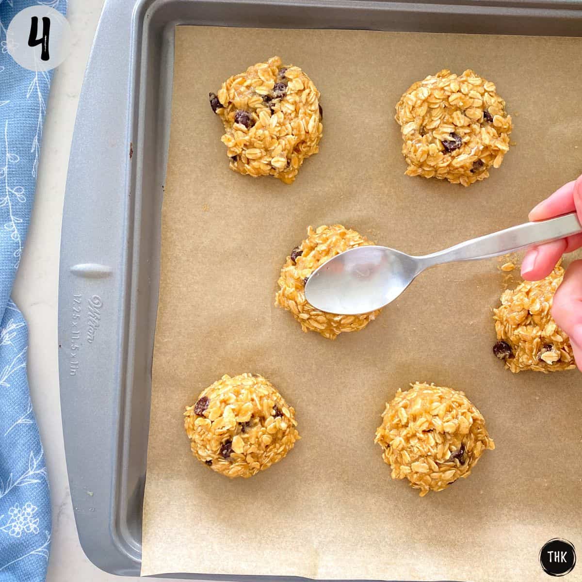 Spoon pressing down cookie on baking sheet.