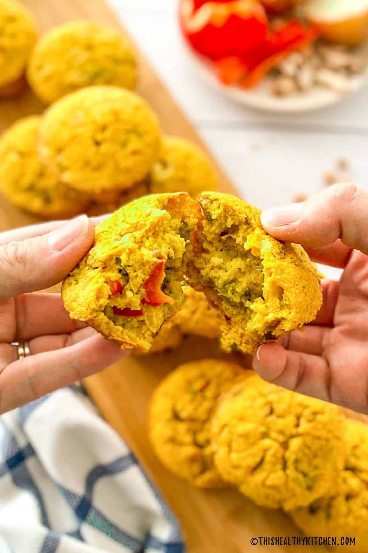 Hands breaking a vegan egg muffin in half to show veggies inside.