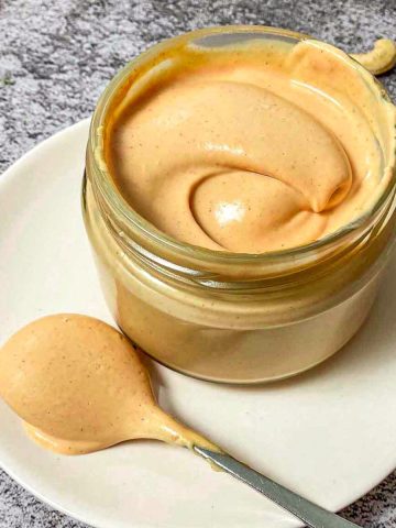 Jar of spicy vegan mayo with spoonful of it beside the jar.