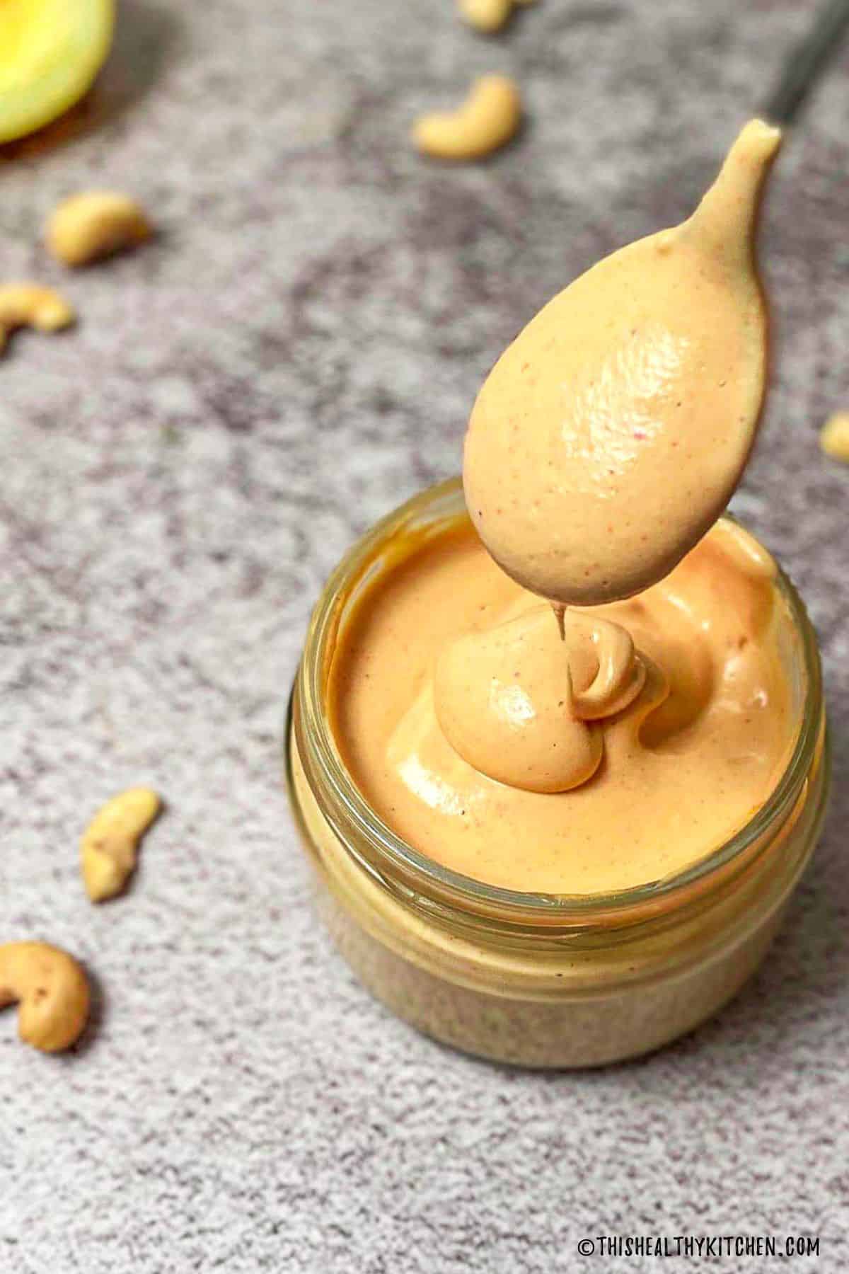 Spoonful of spicy vegan mayo being held above jar of mayo.