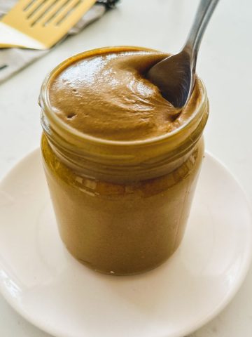 Jar of pistachio butter with spoon inside.