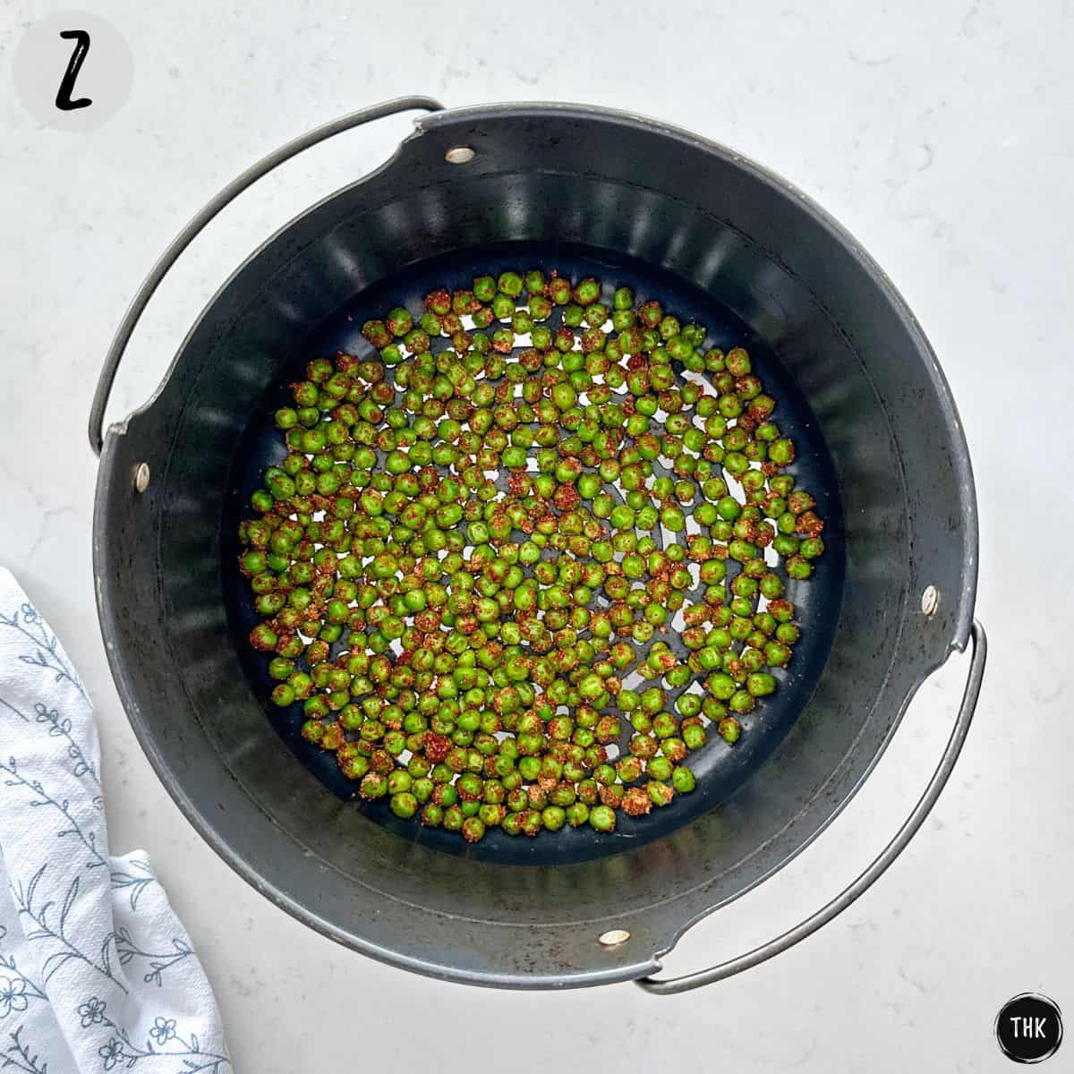 Seasoned peas in a single layer inside air fryer basket.