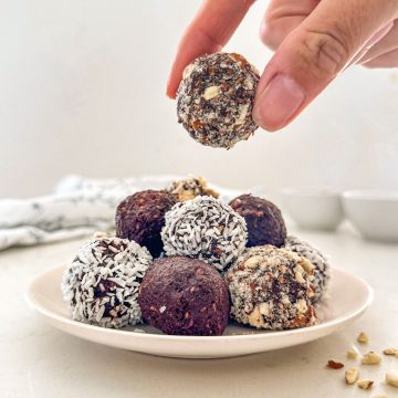 Hand holding up chocolate almond ball above plate with more of them.