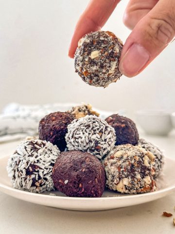 Hand holding up chocolate almond ball above plate with more of them.