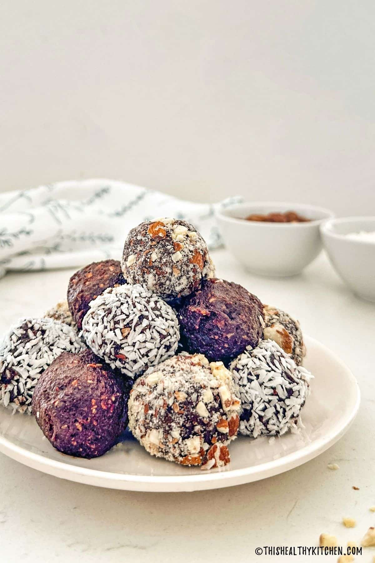 Chocolate balls in white plate with crushed almonds and coconut shreds around them.