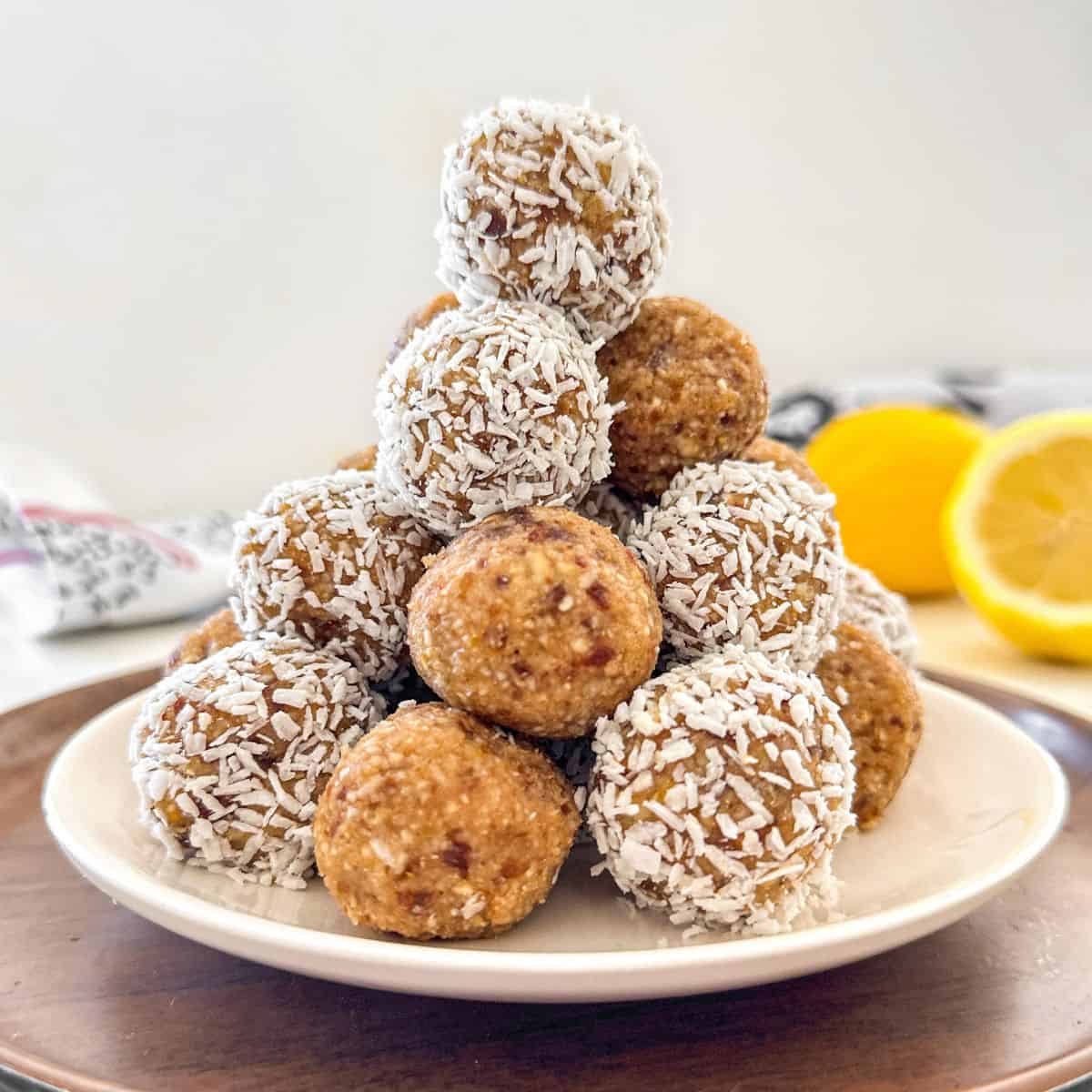 Lemon bliss balls stacked in a pyramid shape on white plate.