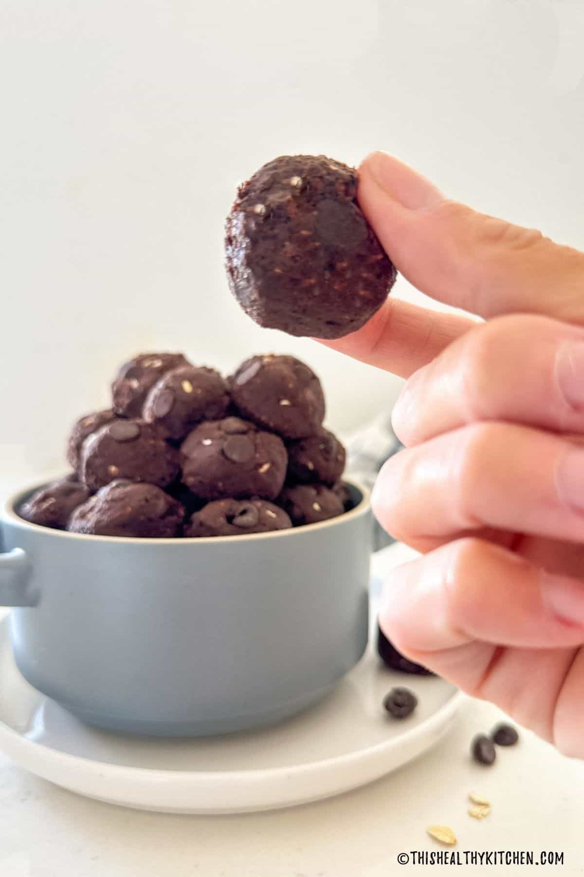 Hand holding up a round chocolate ball with more in the background.