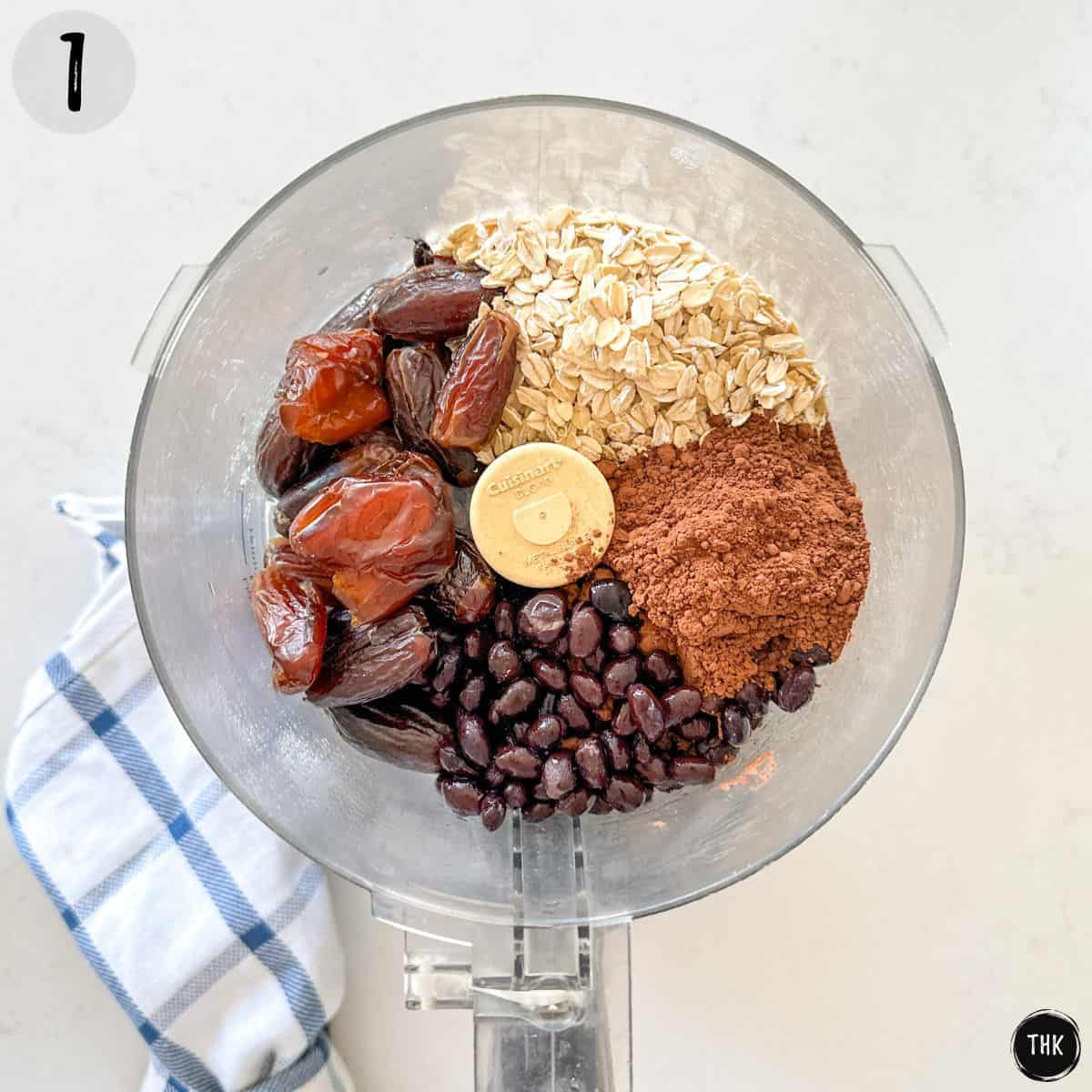 Food processor with oats, dates, black beans, and cocoa powder inside.