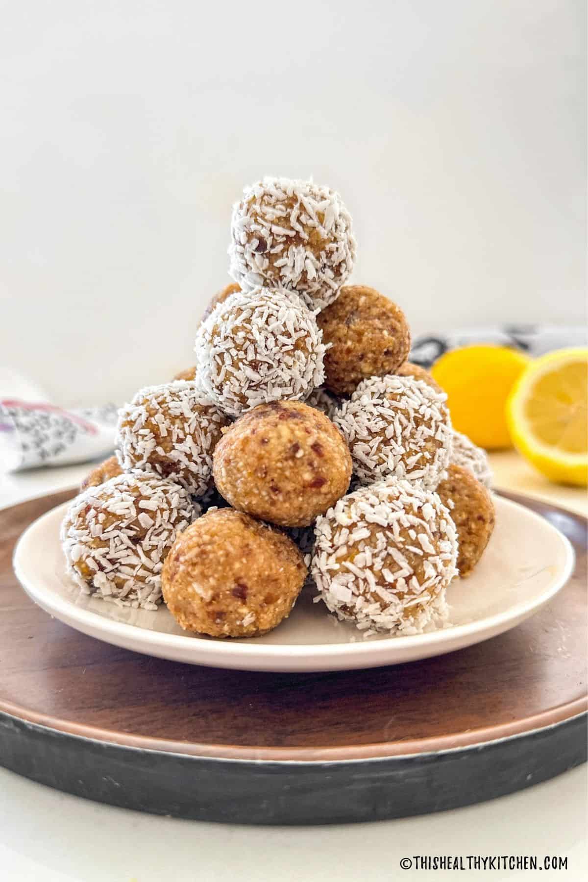 Lemon bliss balls stacked in a pyramid shape on white plate.