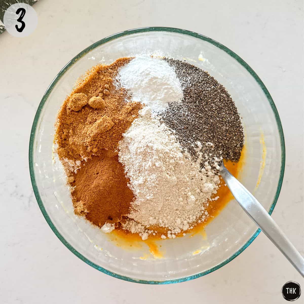 Orange batter with flour, chia seeds, spices and sugar on top in large bowl.