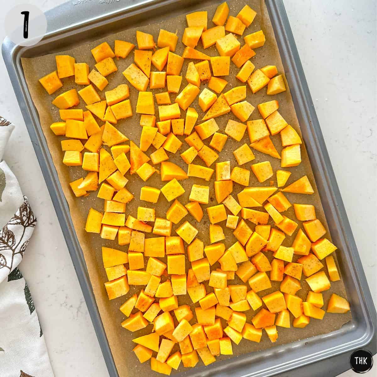 Cubed pumpkin on baking sheet with salt and pepper on top.
