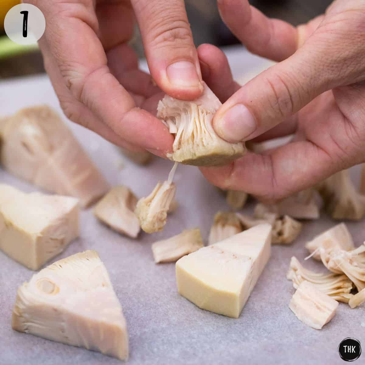 Jackfruit chunks being pulled apart with hands.