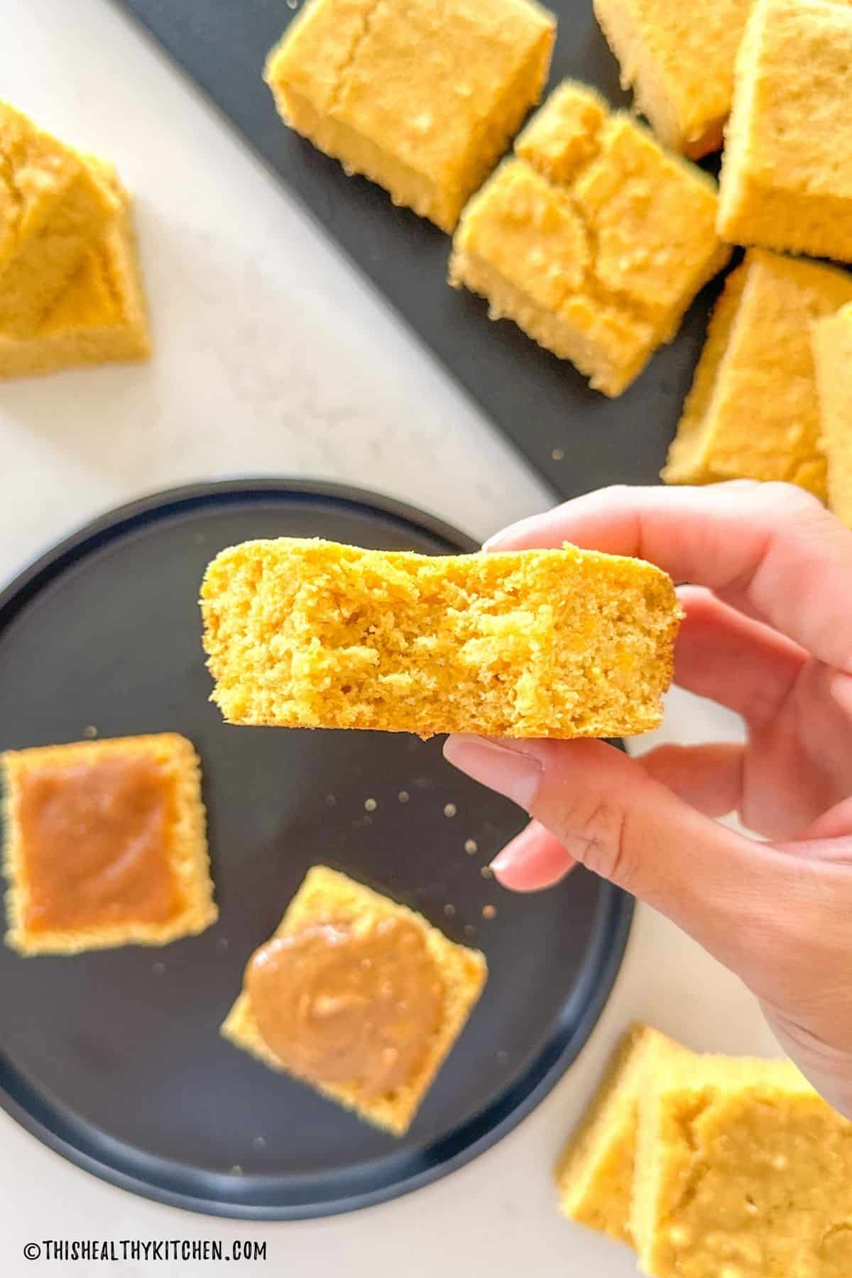 Hand holding up vegan cornbread square with bite taken from it.
