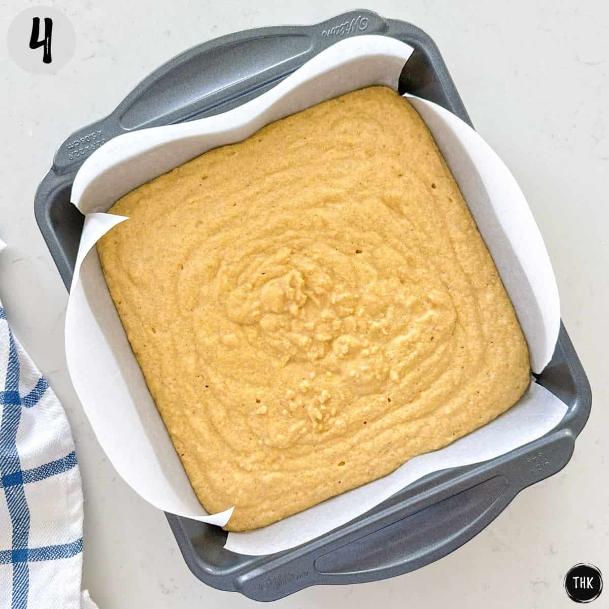 Cornbread batter in square baking pan that's lined with parchment paper.