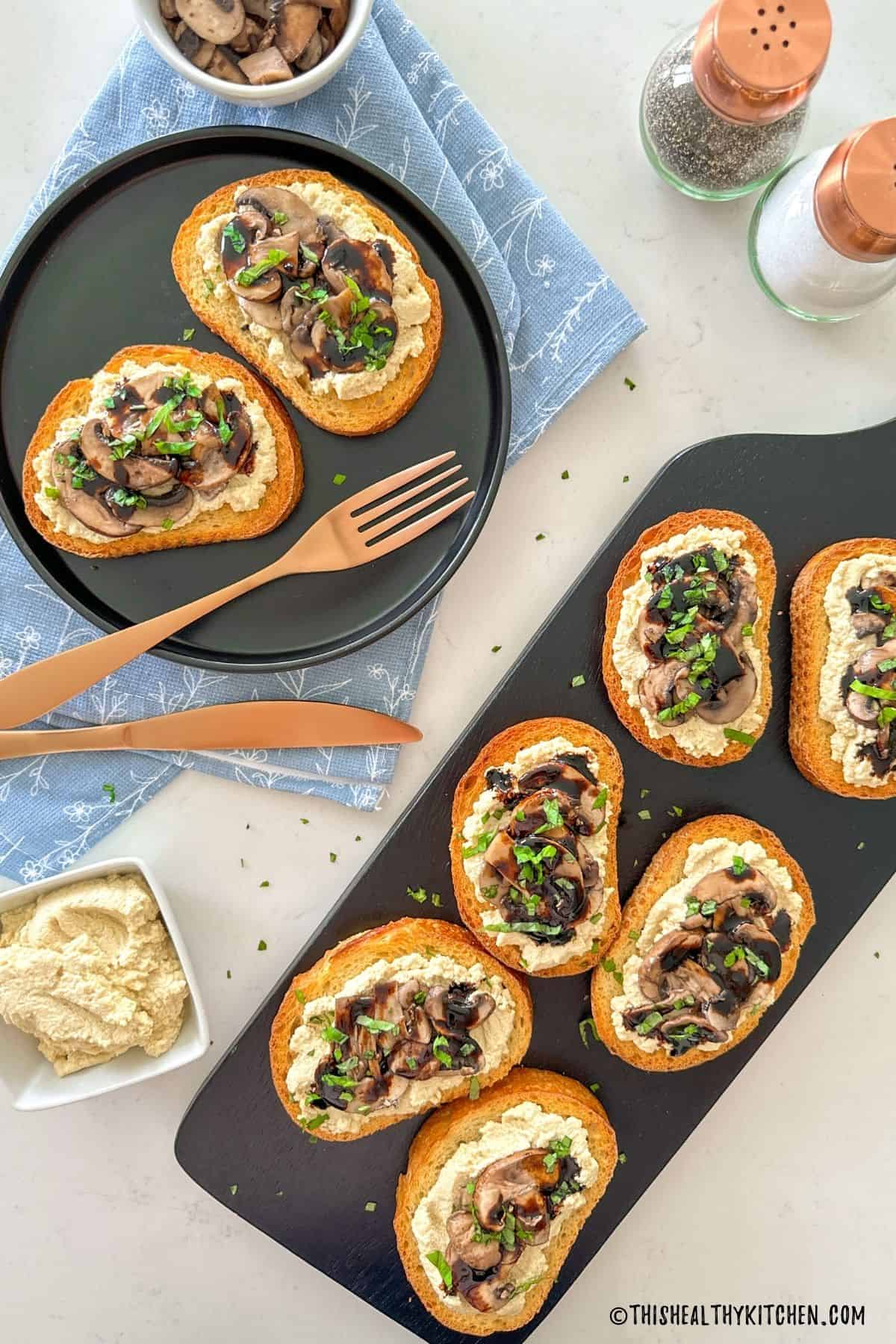 Vegan crostini with ricotta and caramelized mushrooms on cutting board with basil garnish on top.