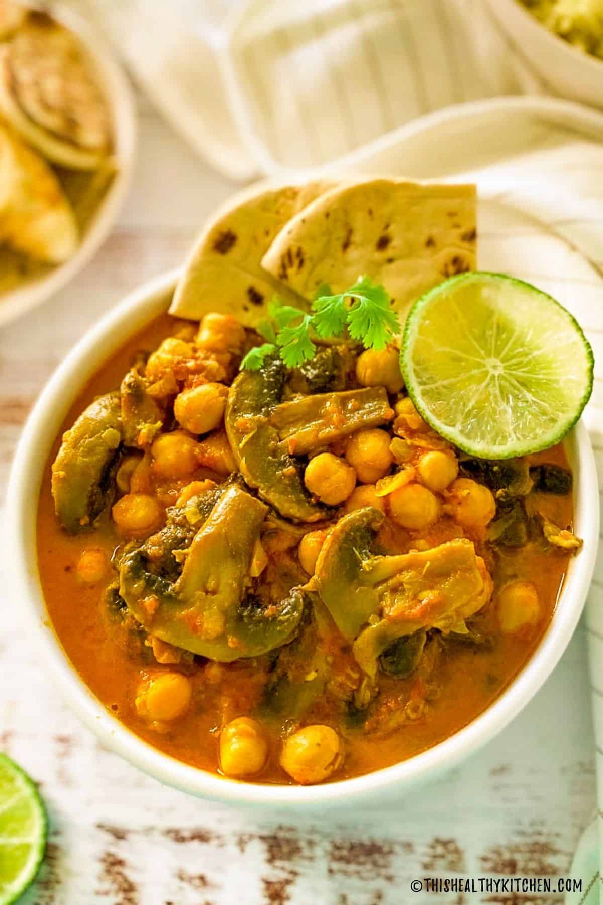 Bowl of mushroom curry with chickpeas, lime, cilantro and pita bread.