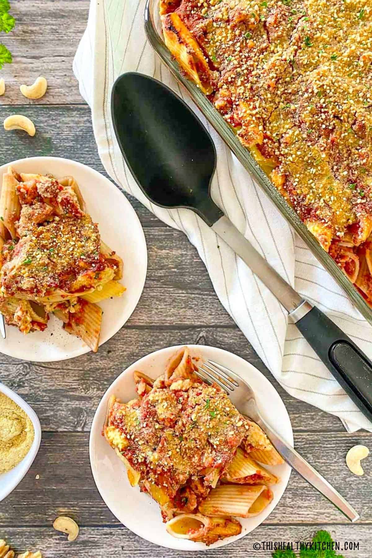 Two plates of baked pasta with vegan ricotta and tray beside them.