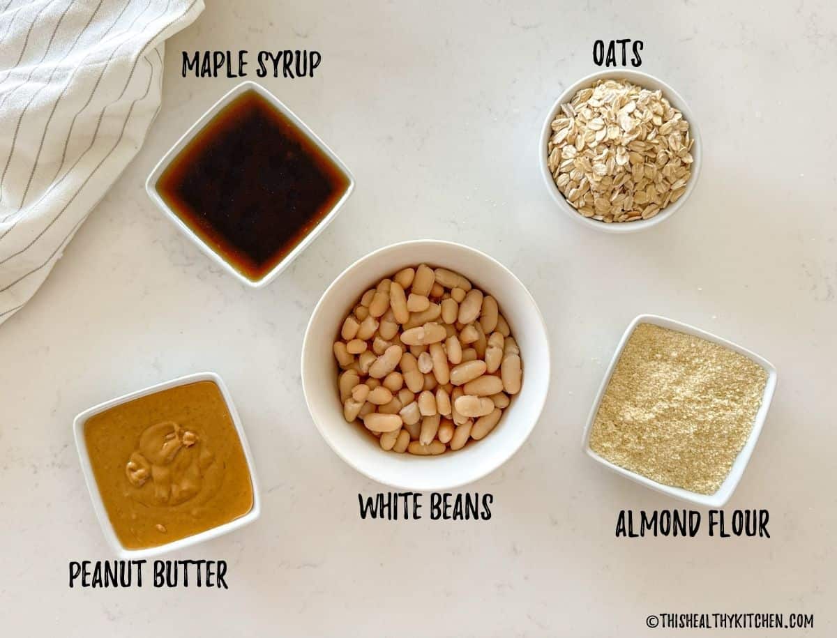Bowls of peanut butter, maple syrup, white beans, oats, almond flour on kitchen countertop.
