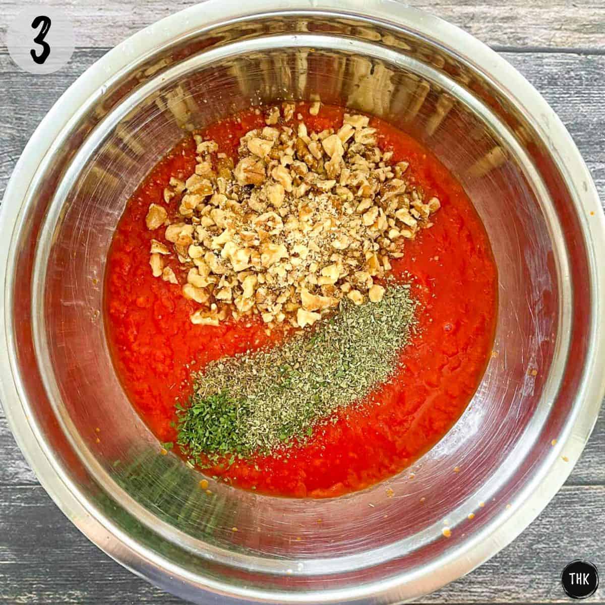 Tomato sauce with crushed walnuts and spices on top in mixing bowl.