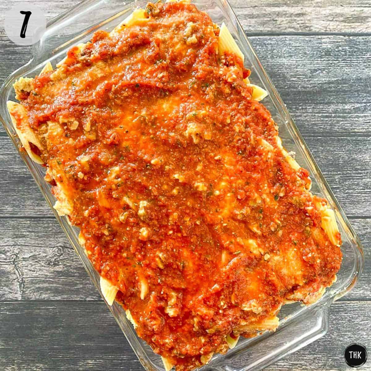 Lasagna tray with cooked rigatoni, vegan cheese and tomato sauce on top.