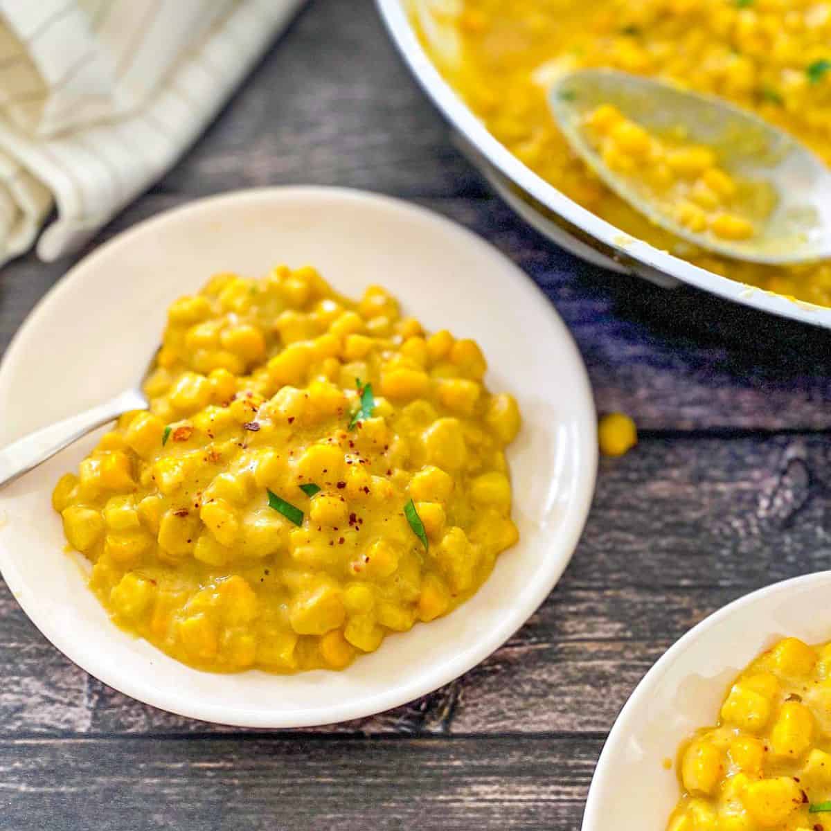 Vegan creamed corn in white plate with pan of more of it in background.