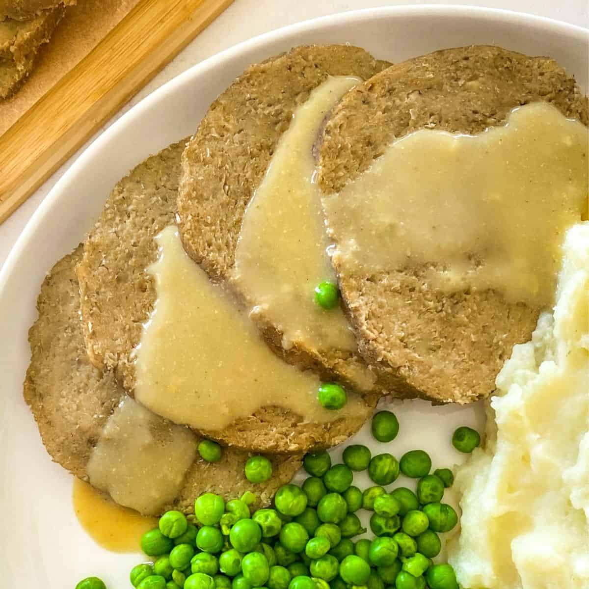 Four slices of vegan roast on a plate with gravy drizzled on top.