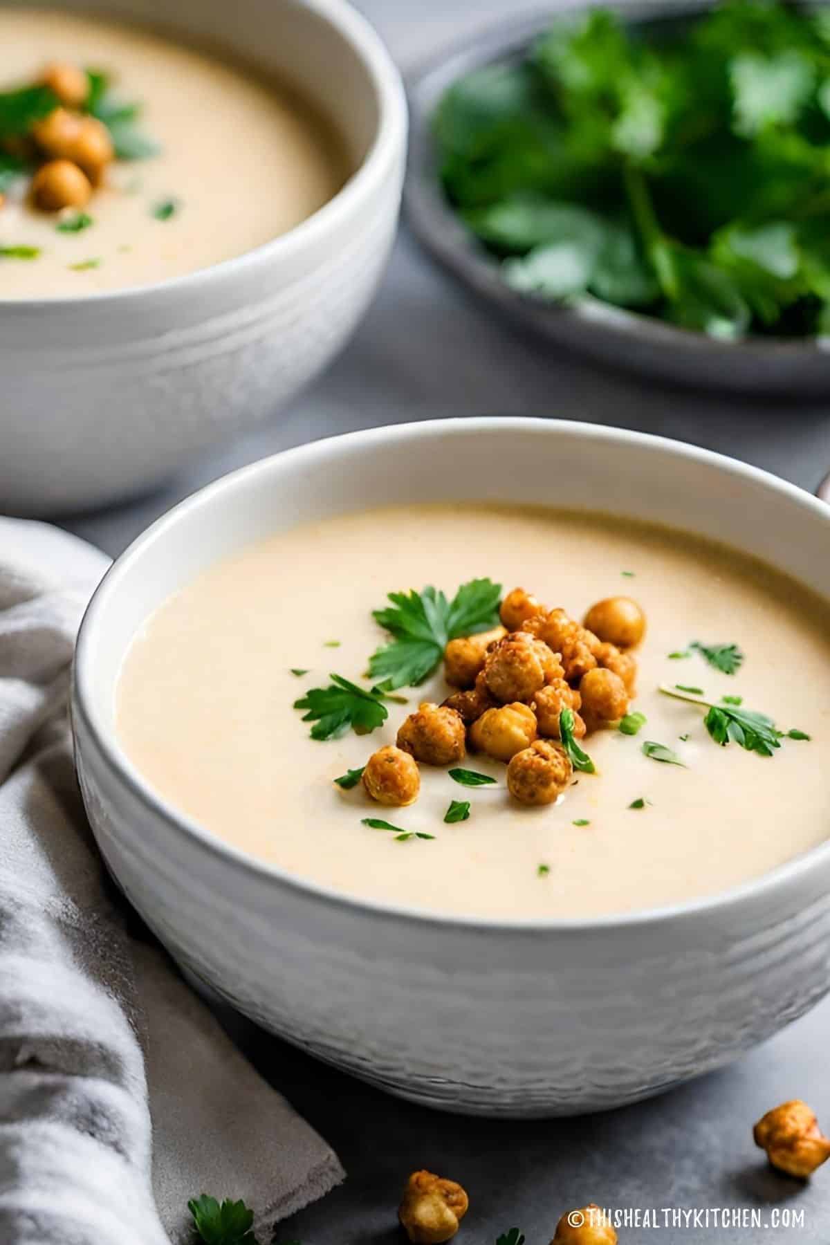 Two bowls of cauliflower soup with roasted chickpeas and cilantro on top.