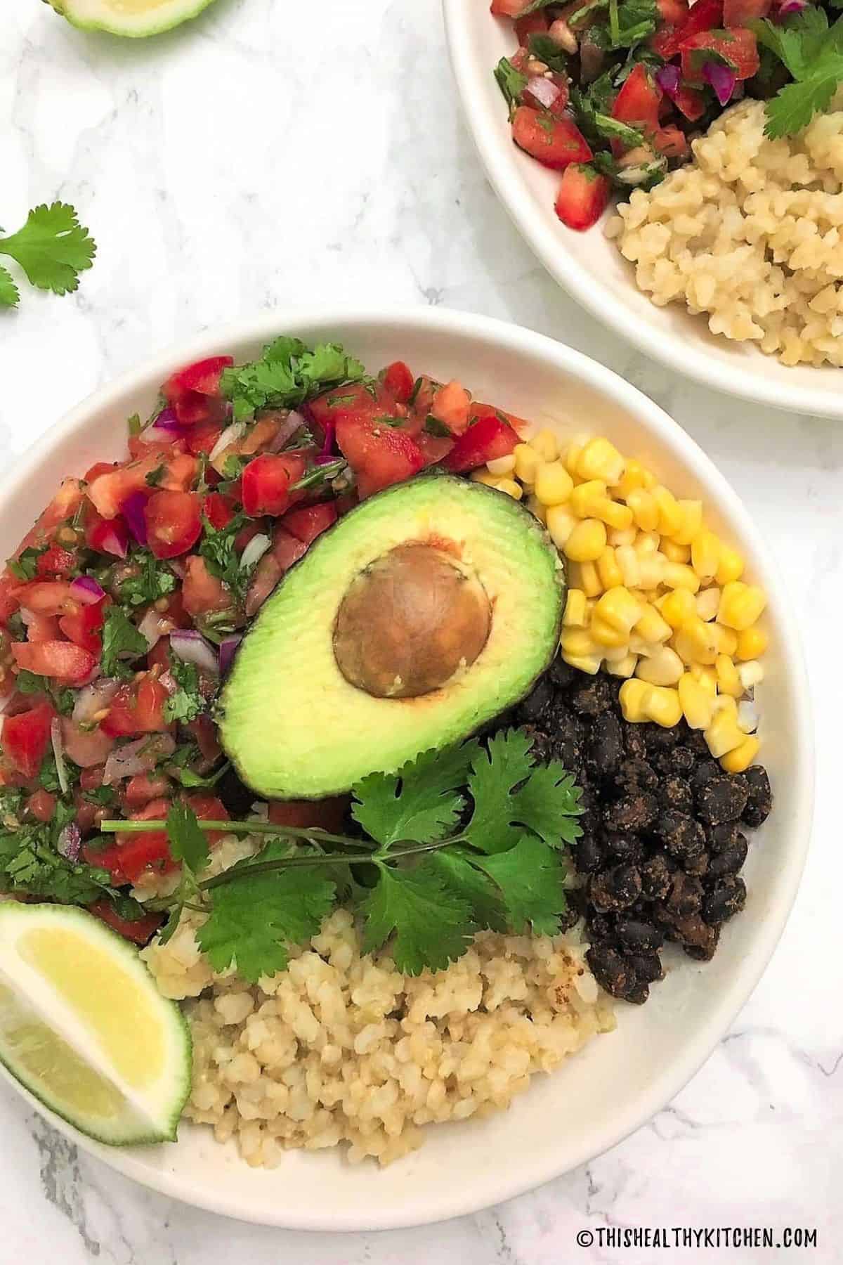 Mexican buddha bowl with rice, beans, corn, tomato salad, avocado and cilantro on top.