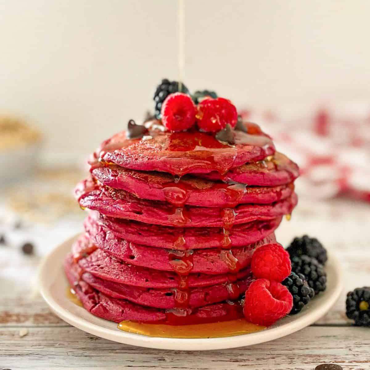 Stack of pink beet pancakes on plate with syrup dripping down the sides.