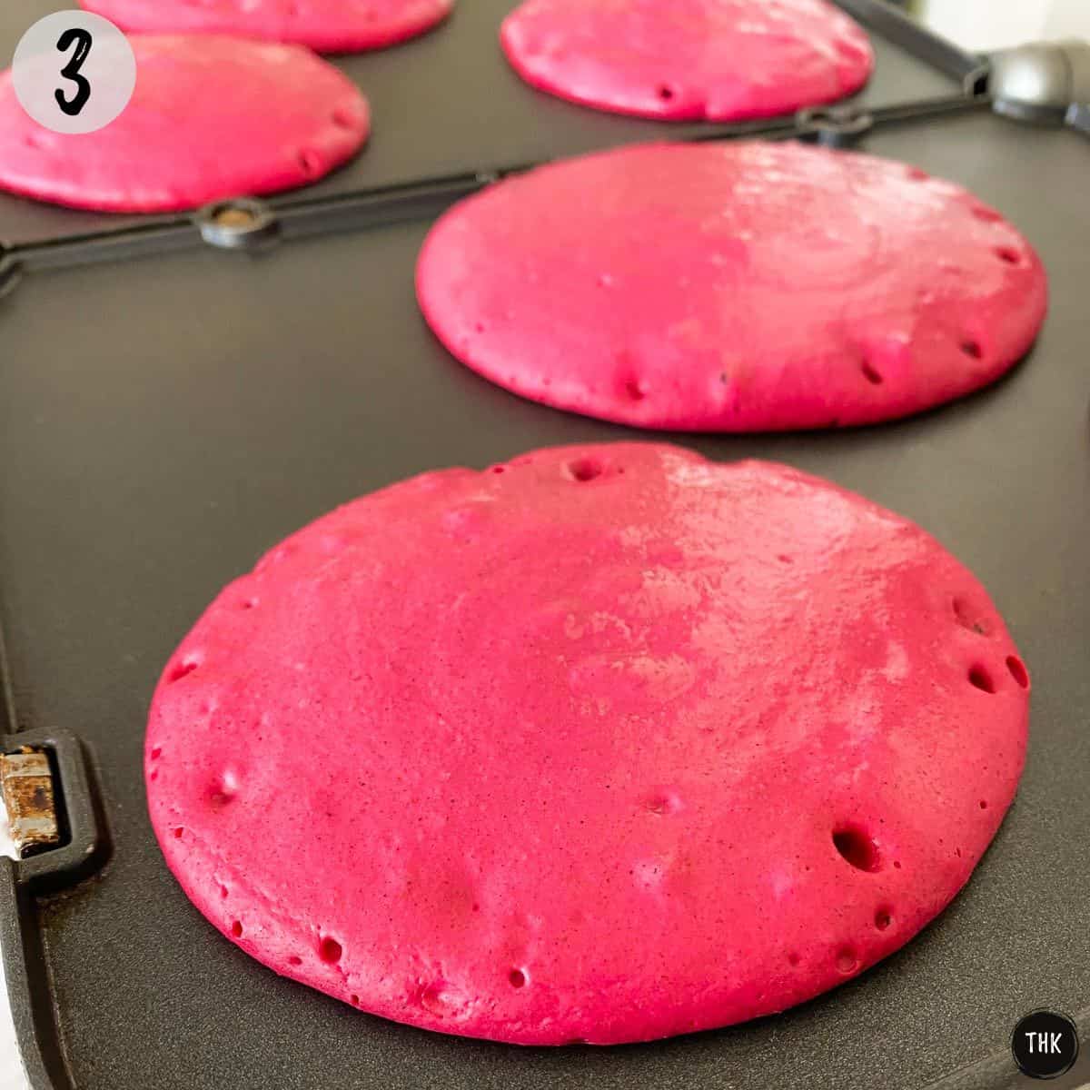 Pink pancakes cooking on griddle.