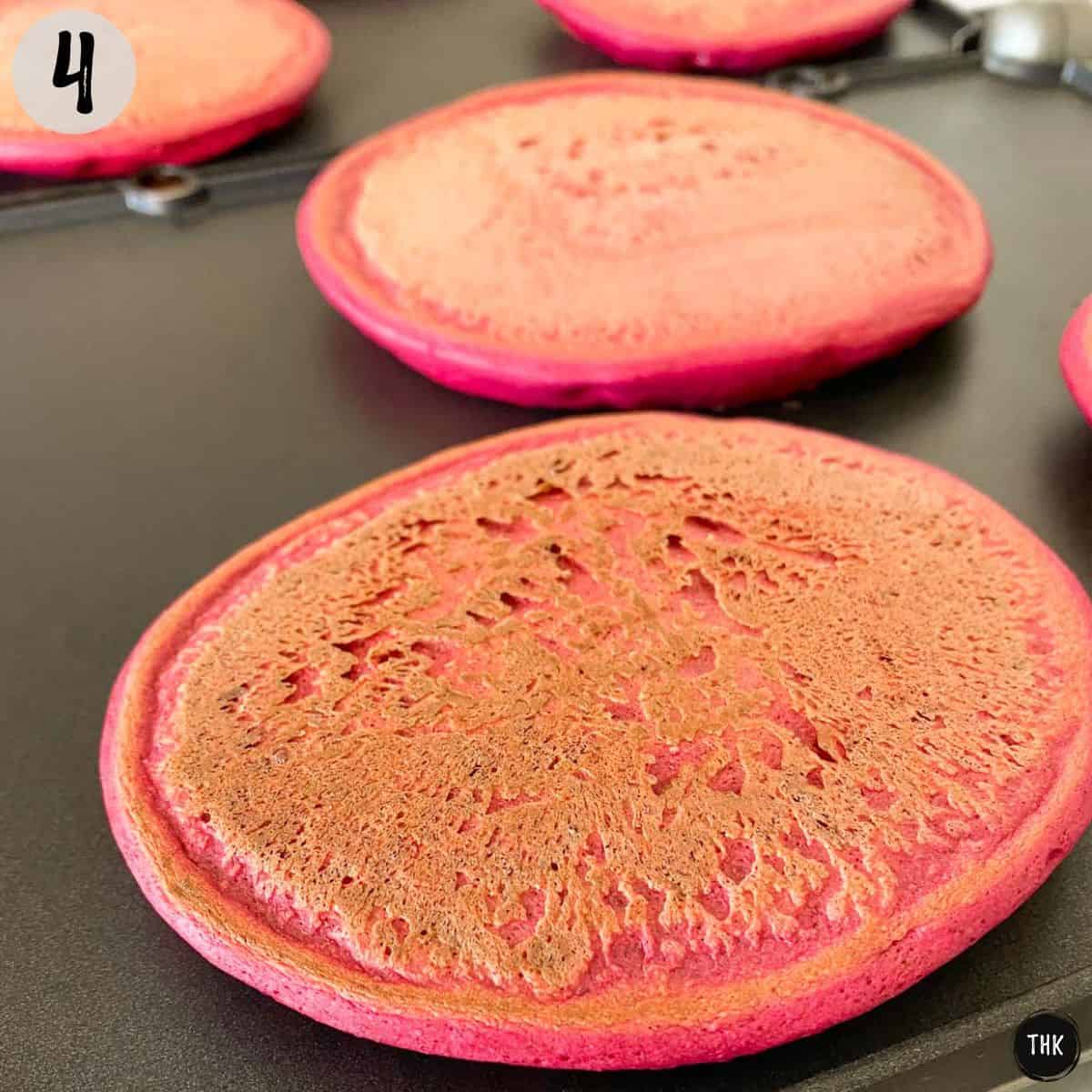 Pink pancakes cooking on griddle.