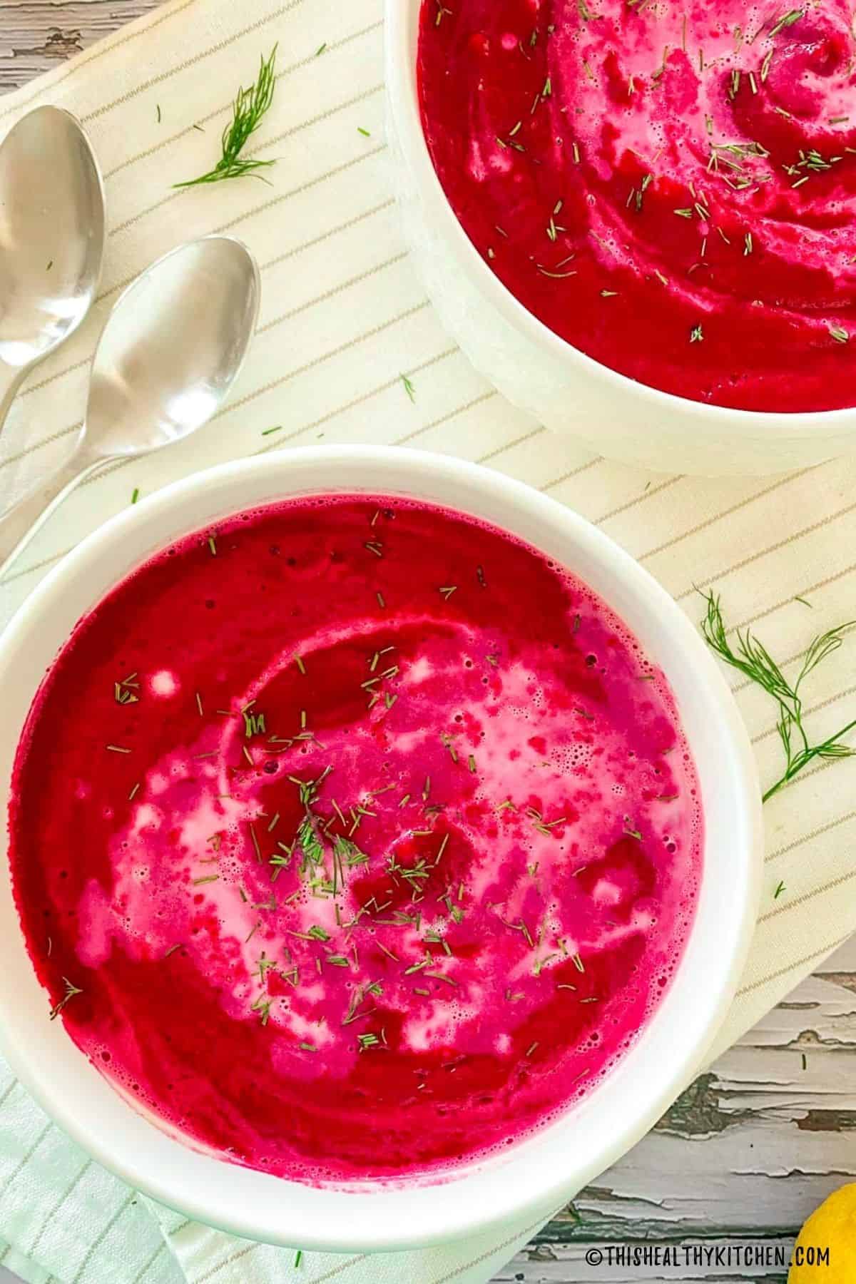 Two bowls of bright pink beet soup with fresh dill on top.