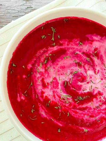 Bowls of bright pink beet soup with fresh chopped dill on top.