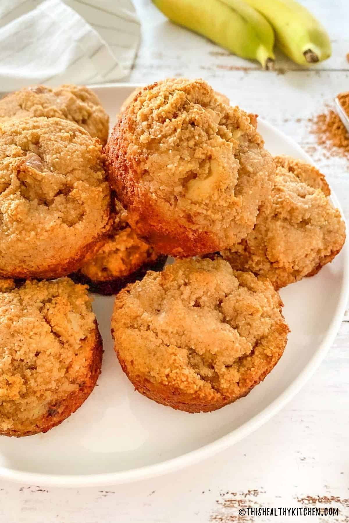 Banana bread muffins on white plate with bananas in the background.